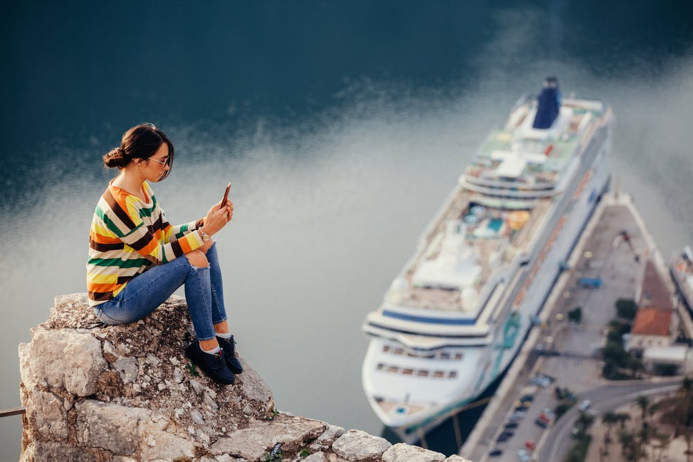 Girl using cell phone with cruise ship in background.
